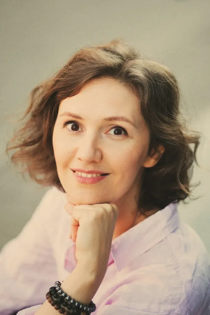 Natalia Dichkovska resting her chin on her hand, smiling softly in warm studio light.