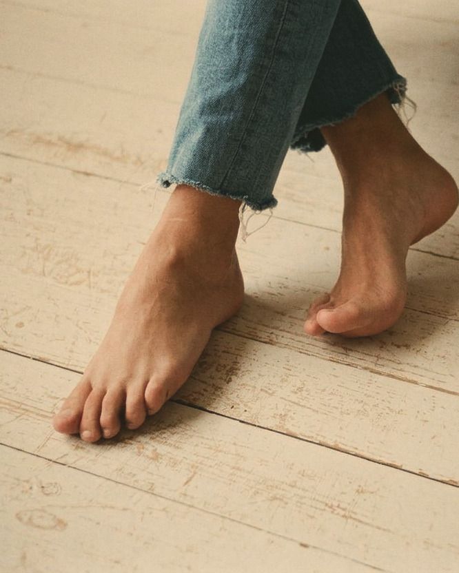 Close crop of bare feet stepping across a worn wooden floor, jeans rolled at the ankle.