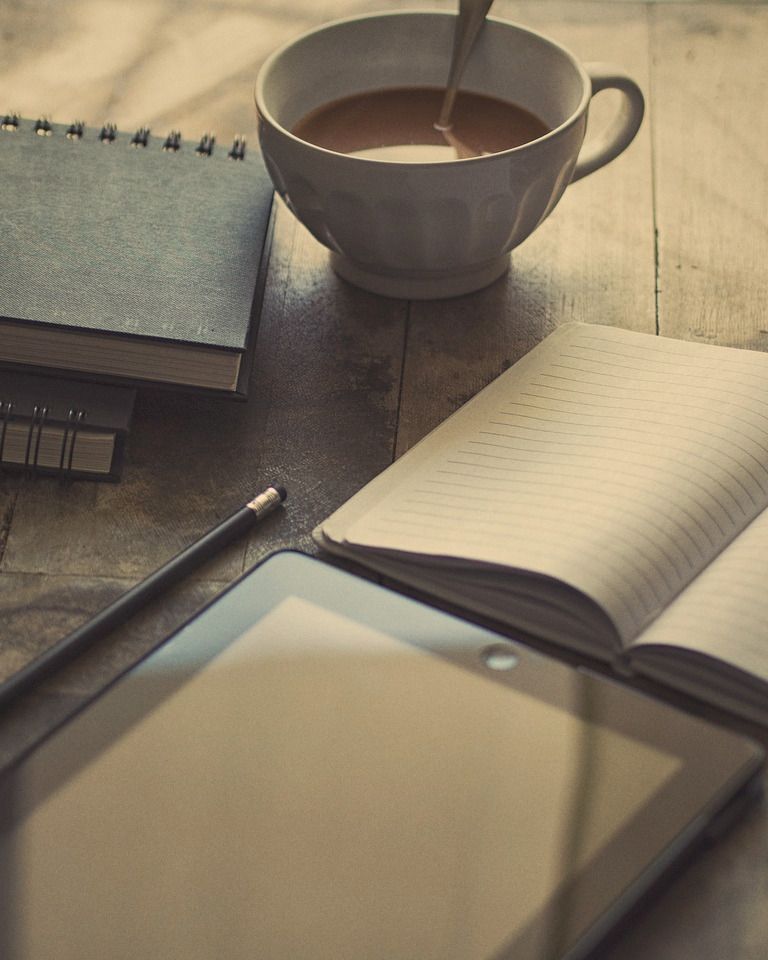 An open lined notebook, a pen and a cup of coffee on a wooden desk, morning light.