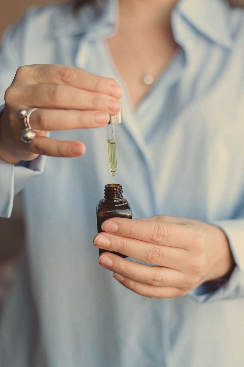 Hands holding a small amber bottle of oil, lifting the glass dropper out of it.