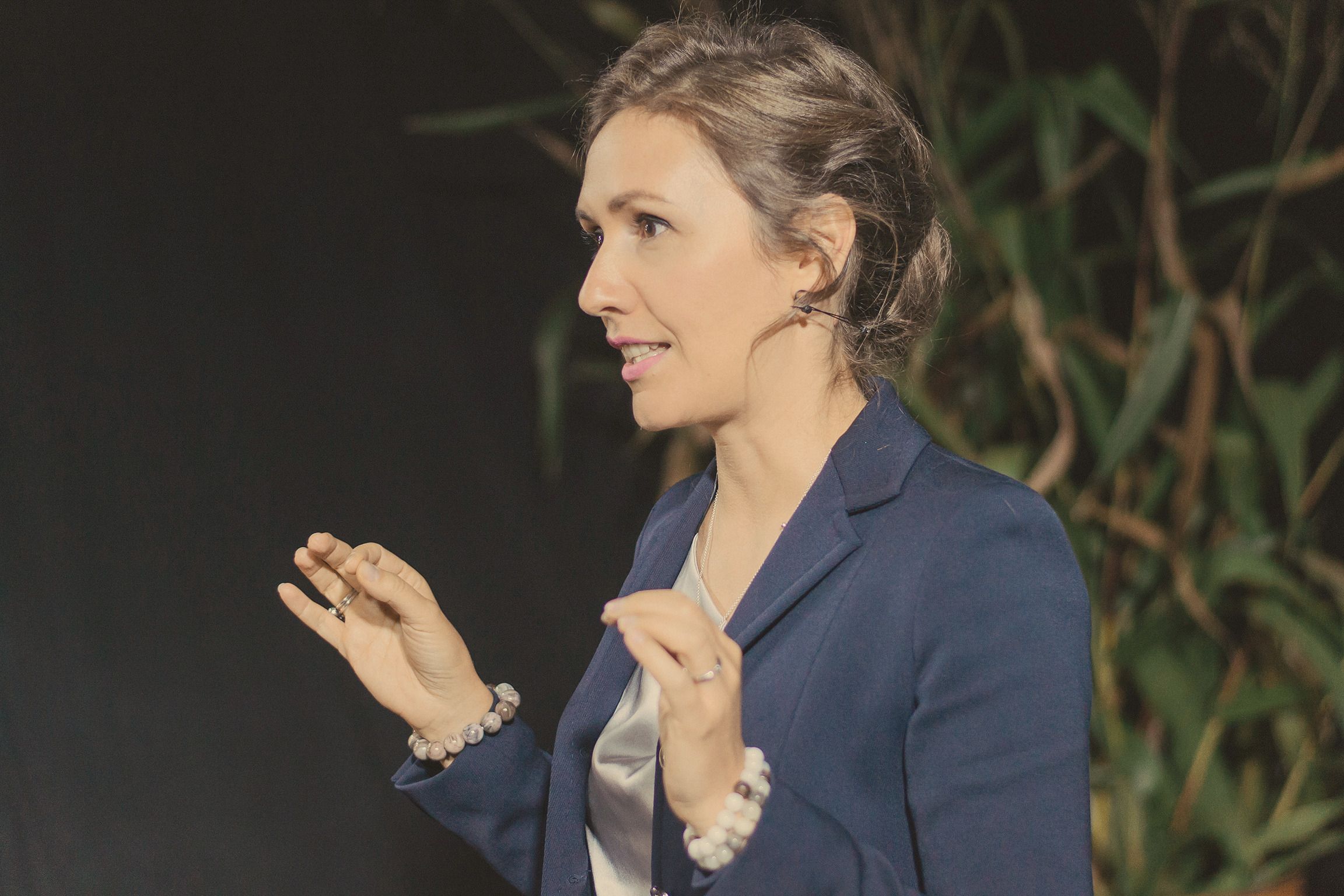 Natalia Dichkovska mid-sentence in a navy blazer, hands raised as she speaks, against a dark stage backdrop.