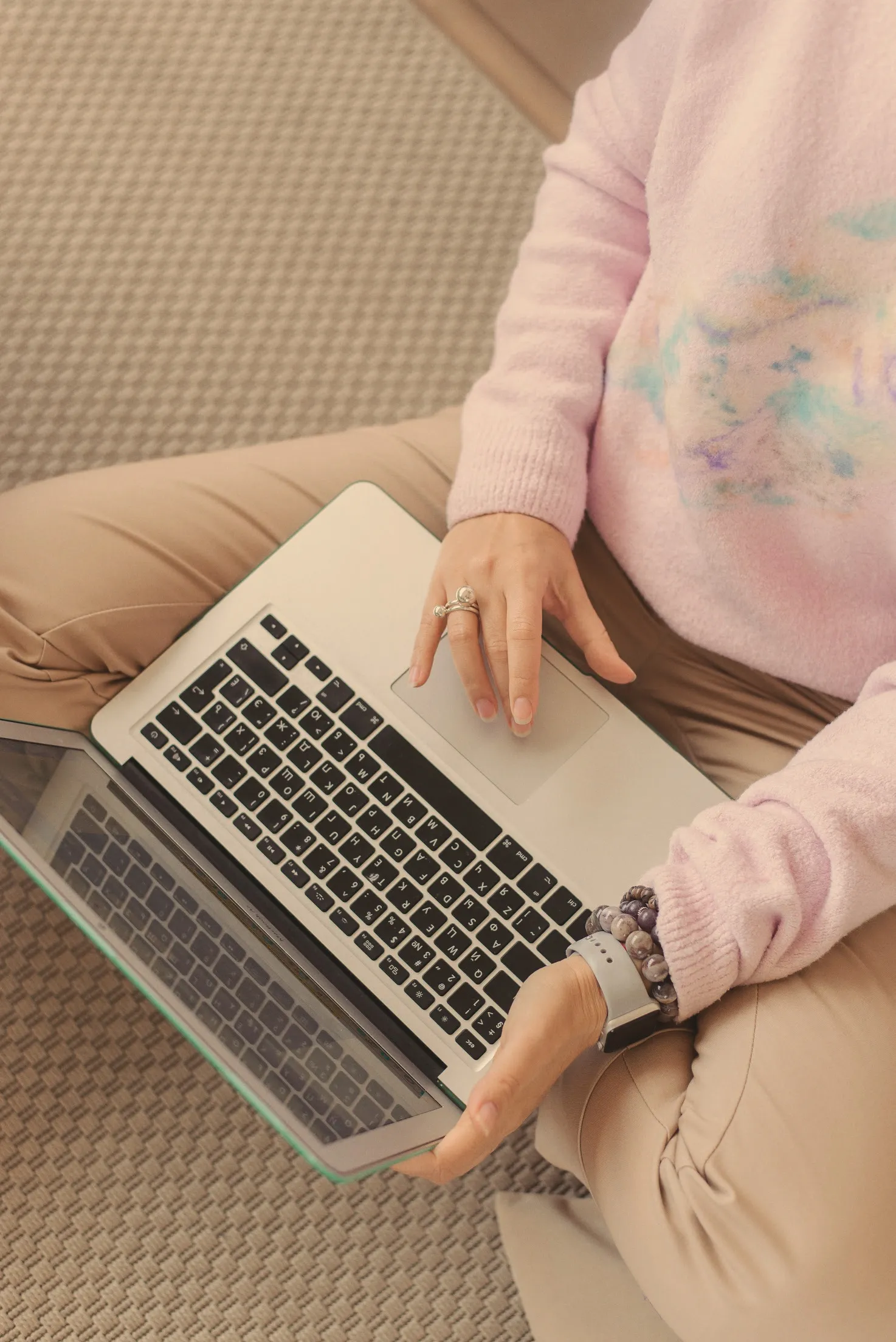 Overhead view of a woman working at a laptop on her lap in daylight, one hand on the trackpad.