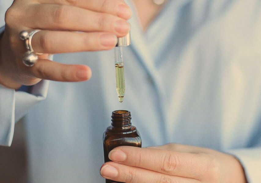 Close-up of hands lifting a glass dropper of golden oil out of a small amber bottle.