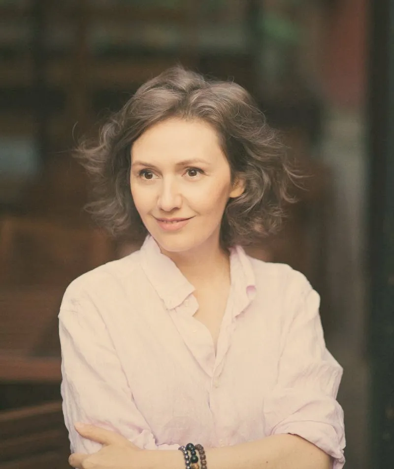 Natalia Dichkovska in a pale lilac linen shirt, arms crossed, smiling slightly in soft outdoor light.