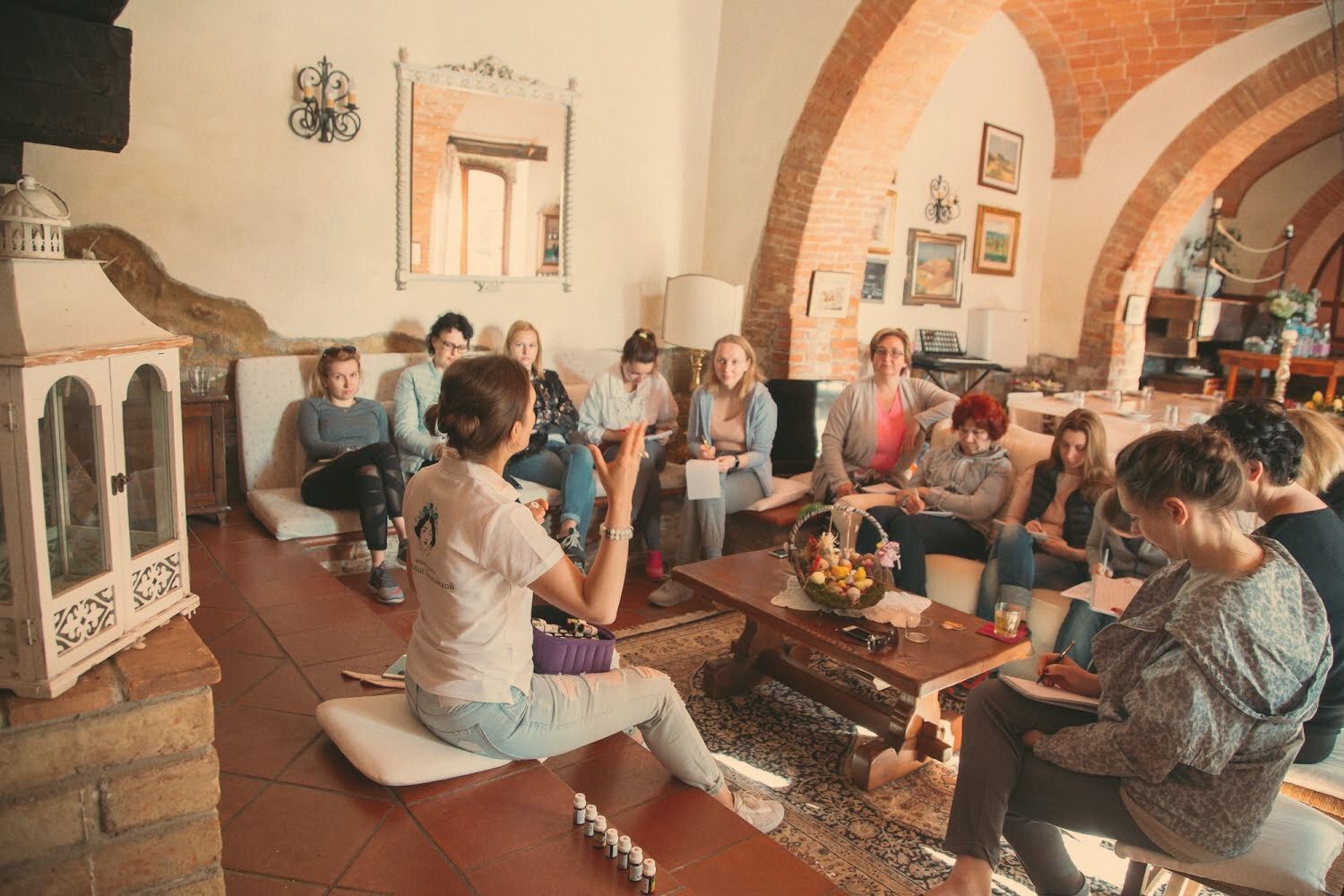 A small group seated in a sunlit room with brick arches, mid-session around a low table.