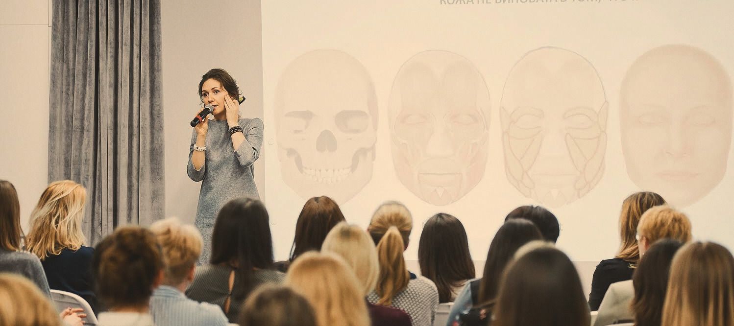 Natalia presenting facial anatomy slides to a seated audience.