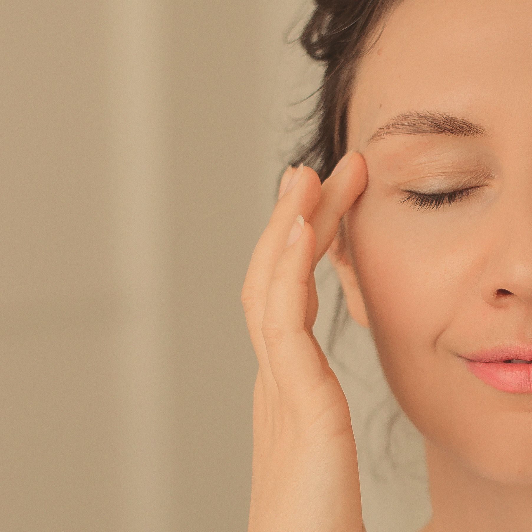 Close crop of a woman's face, eyes closed, fingertips resting at her temple.