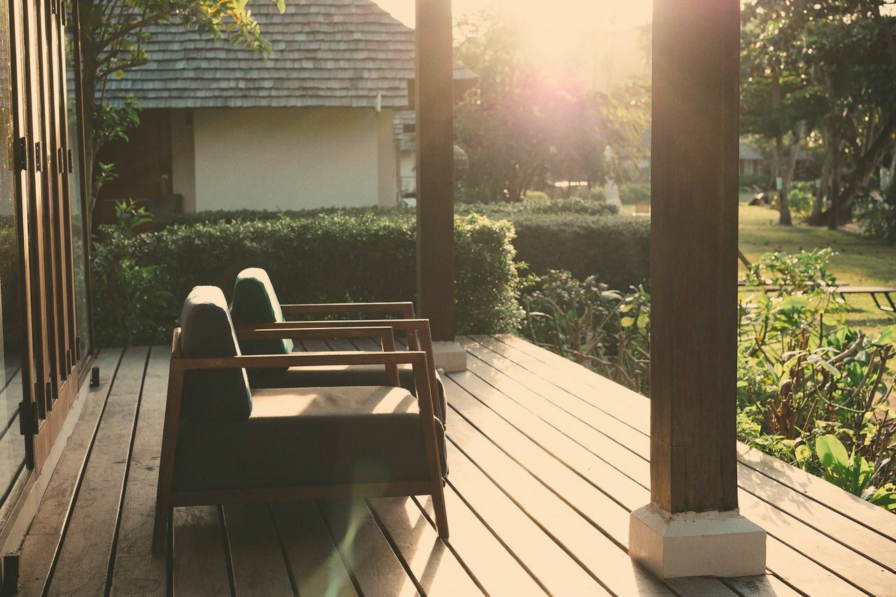 A covered porch with wooden armchairs overlooking a garden in early morning light.